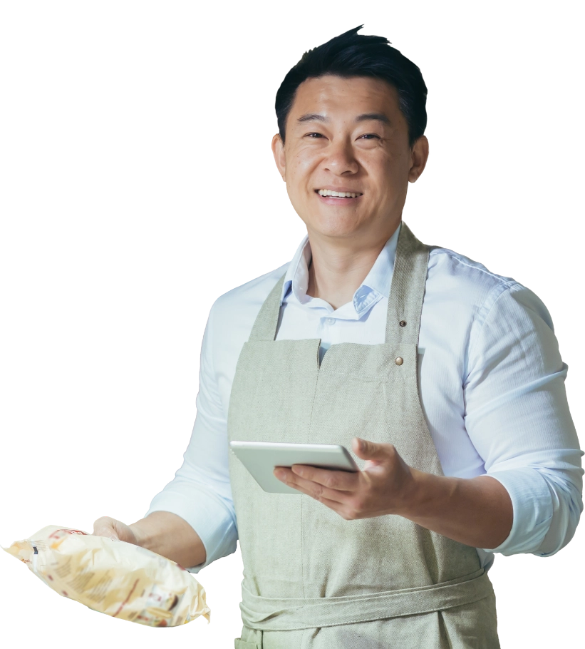 Male wearing an apron holding a food product in one hand and a tablet in the other